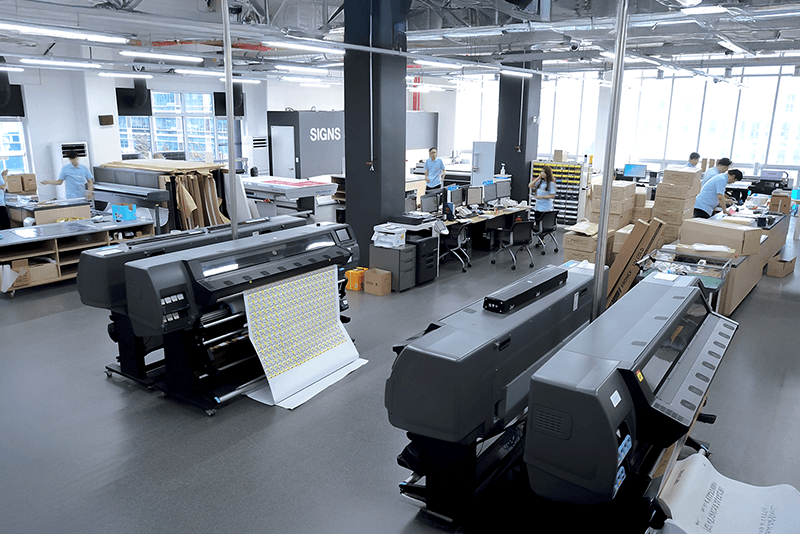 5_센터네트워크_9_킨코스 대형 실사 출력 장비가 설치된 제작 공간, 직원들이 출력물을 점검 중인 모습