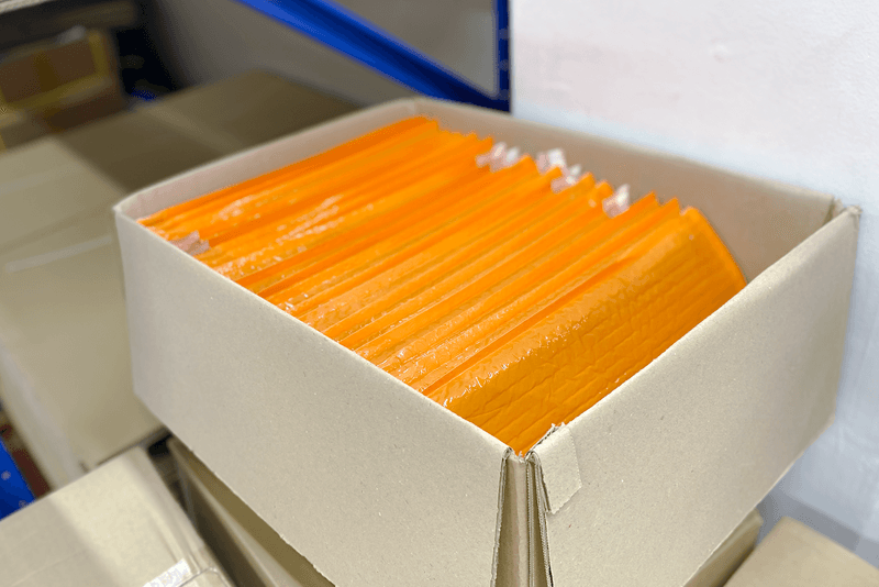 2_포장배송_12_주황색 완충 포장재가 정리된 박스, 소형 인쇄물과 굿즈 포장을 위한 맞춤형 보호 자재 준비 모습