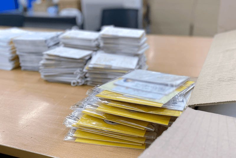 2_포장배송_14_투명 비닐로 개별 포장된 소형 인쇄물 세트가 포장대 위에 놓여 있는 모습, 세트 단위 납품을 위한 세밀한 포장 과정