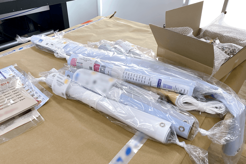 2_포장배송_5_배너, 포스터 등 롤형 인쇄물이 개별 비닐 포장된 상태로 정리된 모습, 매장별 납품을 위한 분할 포장 과정