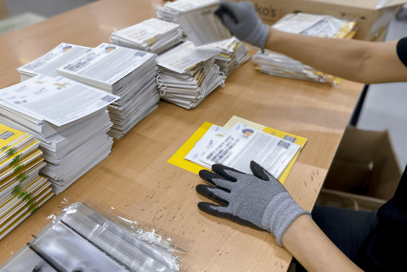 2_포장배송_6_킨코스 직원이 인쇄물을 분류하고 봉투에 담는 장면, 세트 단위 패키징 및 캠페인 물류 준비 과정