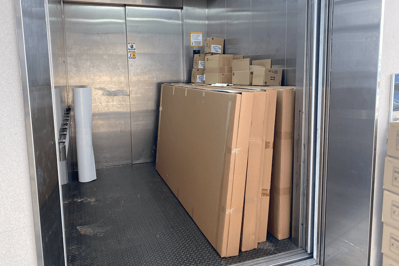 2_포장배송_7_엘리베이터 안에 세로로 세워진 대형 판넬 박스와 납품 박스들이 적재된 모습, 물류 출하 직전 단계의 배송 준비 장면