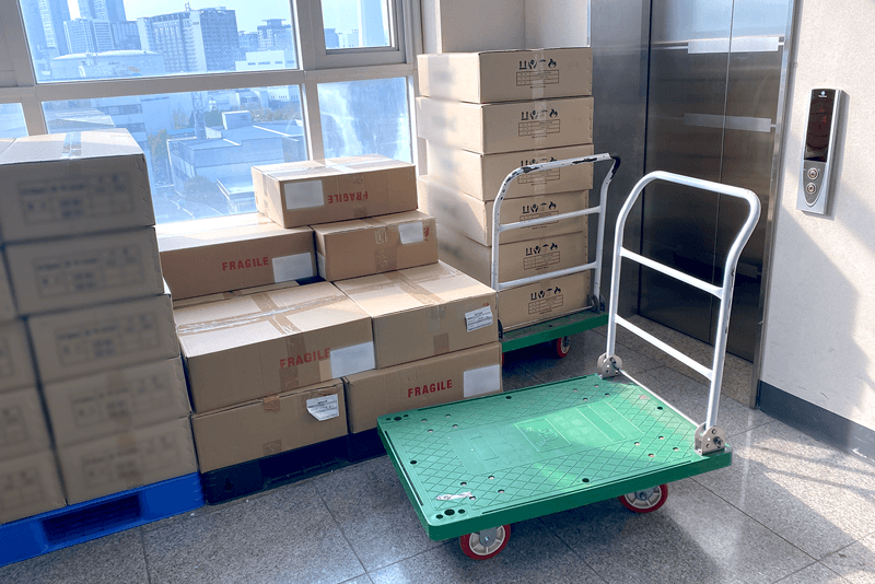 2_포장배송_8_킨코스 물류 구역 내 운반 카트와 적재된 박스 더미, 배송 전 분류 및 이동을 위한 준비 공간