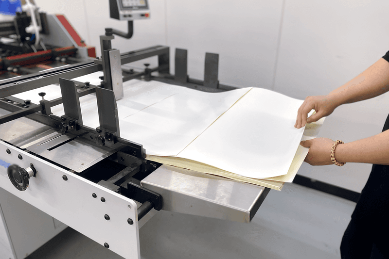 1_생산제작_16_킨코스 직원이 인쇄 공정 중 용지를 정렬하며 품질을 점검하는 장면, 인쇄물 접지 및 후가공 과정의 세밀한 관리 모습.png