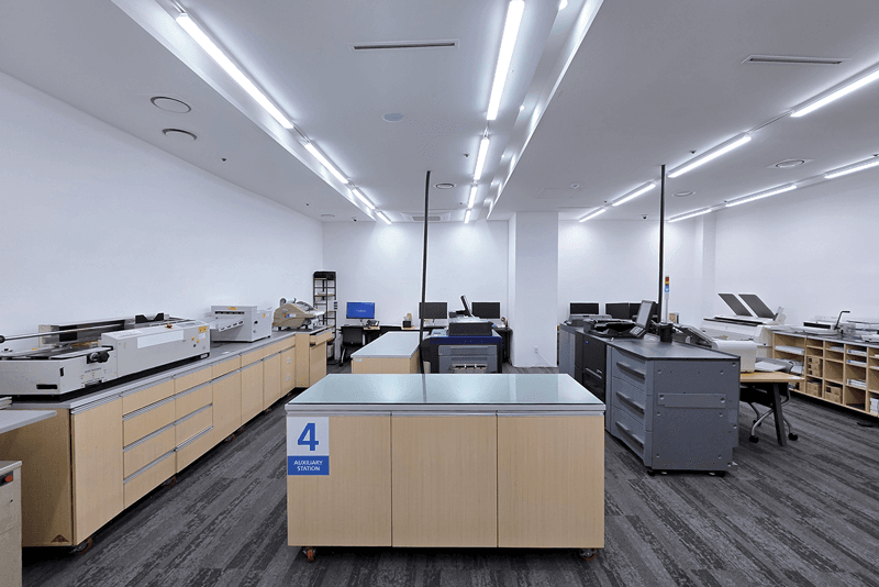 킨코스 직원이 제본된 인쇄물을 검수하고 정리하는 모습, 맞춤 제작물의 품질 확인 및 포장 전 공정 관리 장면