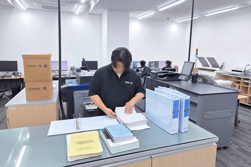 1_생산제작_8_킨코스 직원이 제본된 인쇄물을 검수하고 정리하는 모습, 맞춤 제작물의 품질 확인 및 포장 전 공정 관리 장면