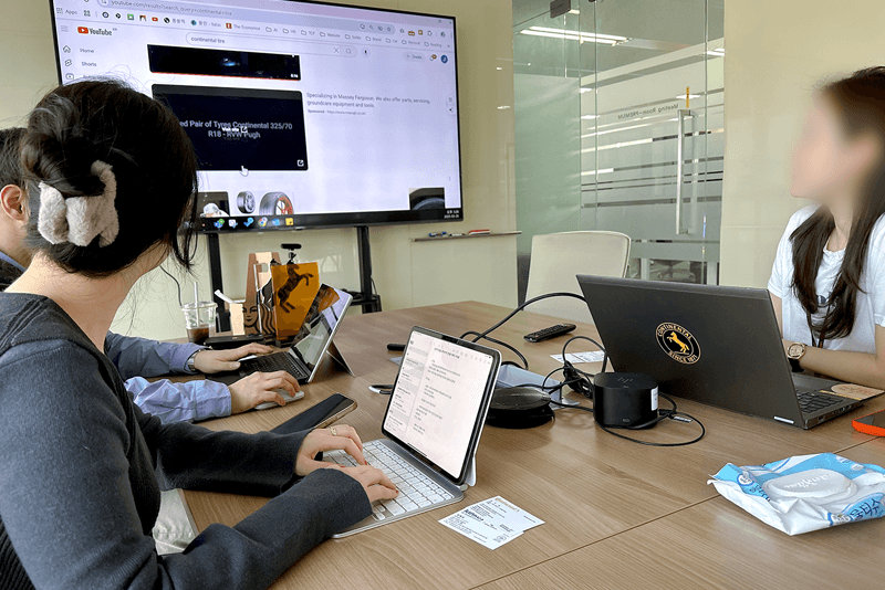 4_인력지원_4_회의실에서 노트북과 대형 화면을 통해 마케팅 영상을 공유하며 회의하는 킨코스 팀원들